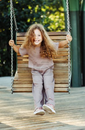 Téléchargez les photos : Une fillette de cinq ans se balance sur une balançoire dans le parc. Bonne enfance. Une belle journée d'été. - en image libre de droit