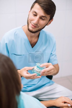 Photo for Male dentist shows dentures with a bracket in her hands to the patient. False teeth in the hands of the follow-up doctor. prosthetic dentistry. Fake teeth. - Royalty Free Image