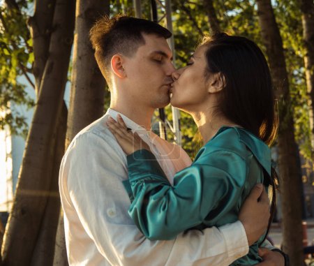 Téléchargez les photos : Jeune couple heureux amoureux de différentes nationalités embrassant et embrassant dans le parc. Femme asiatique et homme européen. Bonne heure d'été. - en image libre de droit