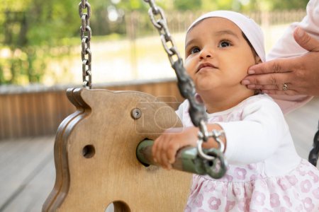 Photo for Little smiling baby girl sits on a swing in the park on a summer day, time for games, happy summer. - Royalty Free Image