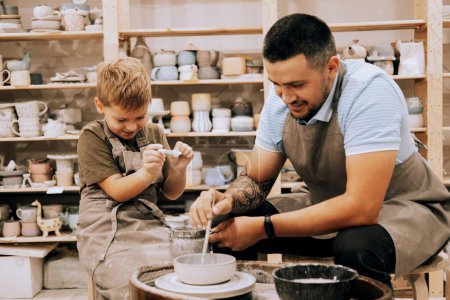 Photo for Pottering with son. Confident young man and little boy making ceramic pot on the pottery class. Lifestyle concept. - Royalty Free Image