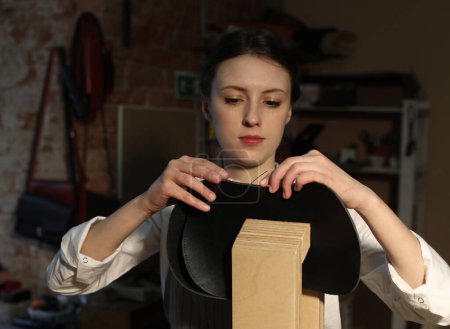 Photo for Young woman works in a workshop, sews leather bags - Royalty Free Image
