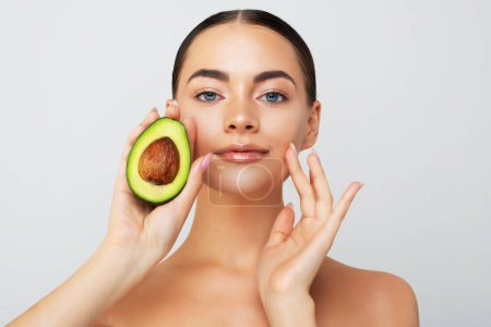 Photo for Beauty portrait of young topless woman showing halved avocado standing isolated over white background - Royalty Free Image