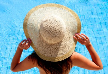 Photo for Young sexy woman wearing hat in the pool, back niew, summer day - Royalty Free Image