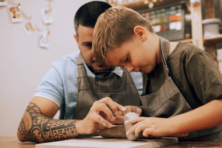 Photo for Pottering with son. Confident young man and little boy making ceramic pot on the pottery class. Lifestyle concept. - Royalty Free Image