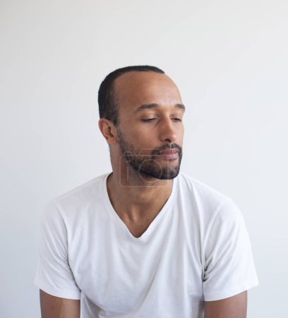 Photo for A young unshaven man wearing white t-shirt on a light gray background. African American. - Royalty Free Image