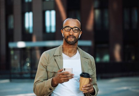Téléchargez les photos : Young afro american man dressed casual holding a cup of coffee to go, smiling happy using smartphone at the city. Lifestyle and people concept. - en image libre de droit