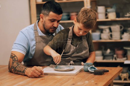 Foto de Papá e hijo se dedican a la creatividad en el taller de cerámica. Pinta un plato casero. Concepto de estilo de vida. - Imagen libre de derechos