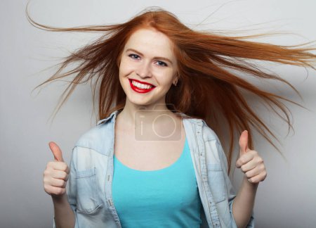 Photo for Successful smiling ginger woman with long hair gives thumb up with two hands - Royalty Free Image