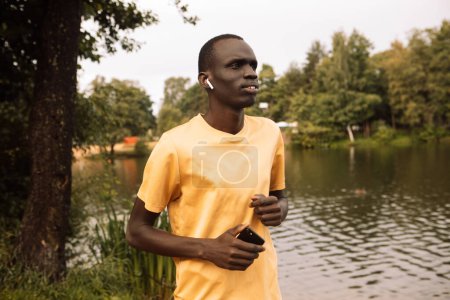 Foto de Un joven negro corriendo cerca de un lago con cabezas. Buenos días. Día de verano. Estilo de vida y concepto deportivo. - Imagen libre de derechos