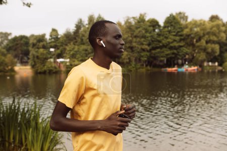 Foto de Un joven negro con una camiseta amarilla está trotando cerca de un lago. Buenos días. Día de verano. - Imagen libre de derechos
