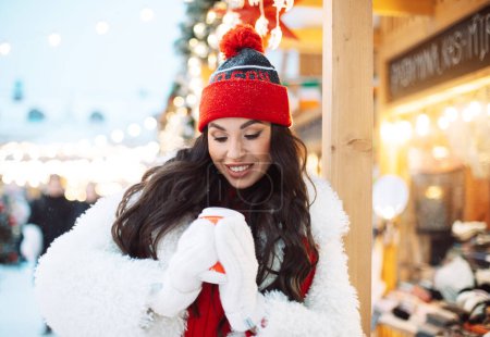 Foto de Hermosa mujer joven feliz en ropa de invierno en el mercado de Navidad bebiendo café. Feliz invierno.. - Imagen libre de derechos