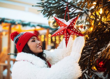 Téléchargez les photos : Joyeux jeune femme à la foire du Nouvel An touche les décorations du Nouvel An sur le sapin de Noël - en image libre de droit
