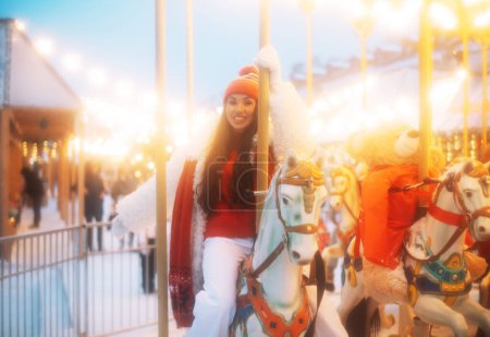 Photo for Laughing young woman at the winter fair riding a horse, carousel, Christmas carelessness and fun. - Royalty Free Image