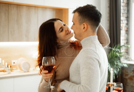 Téléchargez les photos : Jeune couple amoureux buvant du vin rouge à la cuisine. Confortable maison. Amour et romantisme. Mode de vie. - en image libre de droit