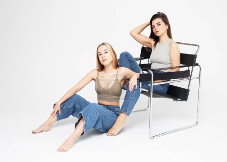 Photo for Lifestyle, friendship, and people concept: Two young female friends with long hair. One woman sitting in the chair, second woman sitting on the floor. - Royalty Free Image