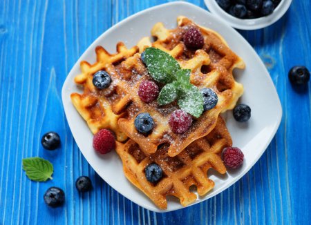 Photo for Waffles with blueberries and raspberries for breakfast on white plate over blue wooden table. Close up. - Royalty Free Image