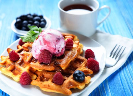 Téléchargez les photos : Gaufres avec crème glacée et framboises pour le petit déjeuner sur une table en bois bleu. Gros plan. - en image libre de droit