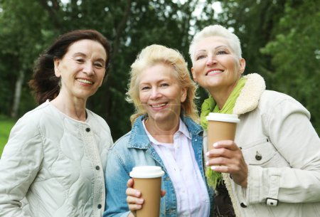 Photo for Lifestyle, emotion, old people and gold age concept. Charming elderly women friends are walking, talking and drinking coffee. Summer day in the park. - Royalty Free Image