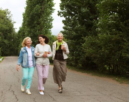Photo for Lifestyle, emotion, old people and friendship concept. Three elderly ladies in casual clothes are walking in the park. Coffee and socializing, friendship in retirement. - Royalty Free Image