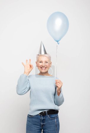 Photo for Portrait of her she nice-looking attractive lovely overjoyed cheerful cheery gray-haired lady holding blue balloon show ok sign isolated on white grey color background - Royalty Free Image