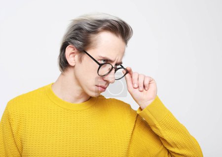 Téléchargez les photos : Un jeune homme en pull jaune et lunettes pose sur un fond gris. Portrait sur fond gris. - en image libre de droit
