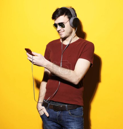 Foto de Sonriente modelo masculino guapo con camiseta casual escucha música con auriculares sobre un fondo amarillo. - Imagen libre de derechos