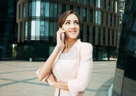 Photo for Beautiful young business woman uses a mobile phone in front of a modern business center. Business, people, tehnology and lifestyle concept. - Royalty Free Image