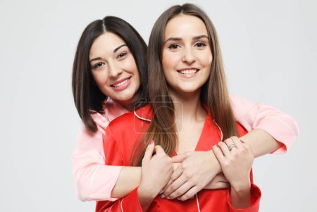 Téléchargez les photos : Style de vie, amitié et concept de personnes - deux belles amies vêtues de pyjama embrassant et souriant sur fond gris - en image libre de droit