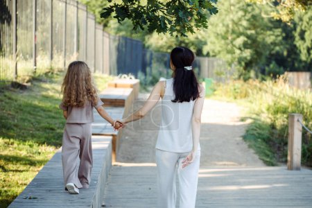 Foto de Una pequeña hija sostiene la mano de su madre. Madre e hija caminan en el parque. Hora de verano, - Imagen libre de derechos