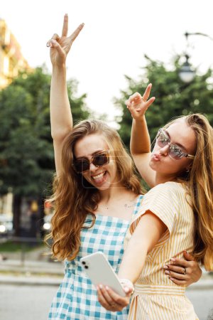 Téléchargez les photos : Deux jeunes femmes heureuses ensemble prenant un selfie dans la ville. Jour d'été. Concept d'amitié. - en image libre de droit