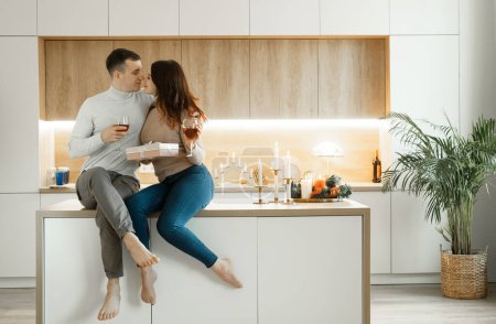 Téléchargez les photos : Jeune couple amoureux buvant du vin rouge à la cuisine. Confortable maison. Amour et romantique. - en image libre de droit