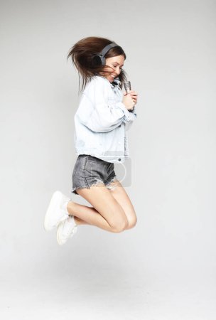 Téléchargez les photos : Femme heureuse avec micro sautant et chantant sur fond gris - en image libre de droit