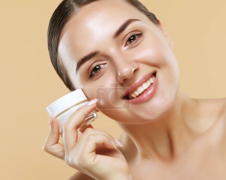 Téléchargez les photos : Concept of using moisturizing cream before going to bed. Beautiful cute pretty charming woman is holding a cream jar isolated on beige background - en image libre de droit