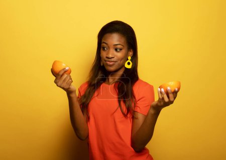 Téléchargez les photos : Jeune afro américaine femme tenir des tranches d'orange regard étonné isolé sur fond de couleur jaune - en image libre de droit