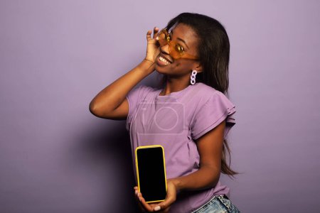 Foto de Retrato de joven afro-americana promotora positiva mostrar teléfono inteligente sobre fondo púrpura - Imagen libre de derechos
