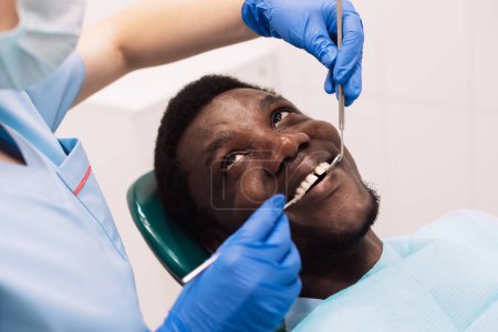 Photo for Portrait of young black male patient getting teeth treatment with dentist. professional stomatologist female using dental drill tool for young man. - Royalty Free Image