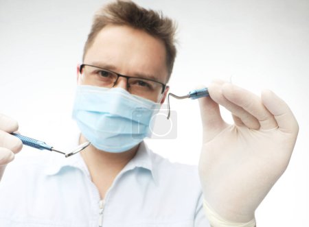 Téléchargez les photos : Jeune dentiste homme en blouse blanche et masque tenant des instruments dentaires sur fond blanc. - en image libre de droit