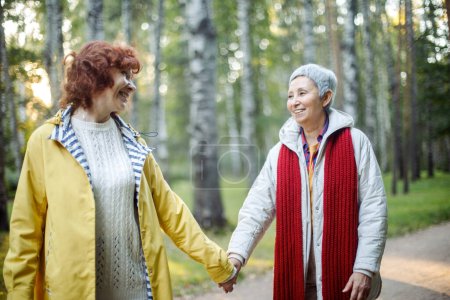 Photo for Cheerful pensioner female friends tallking and laughing in the autumn park. Lifestyle and old people concept. - Royalty Free Image