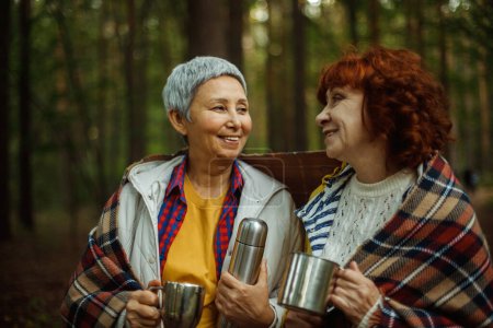 Photo for Two elderly women friends walk in the forest, pour coffee from a thermos, have a great time together, lifestyle concept, - Royalty Free Image