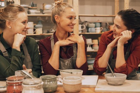 Téléchargez les photos : Une compagnie de trois jeunes amies joyeuses peint des céramiques dans un atelier de poterie. Concept de style de vie. - en image libre de droit