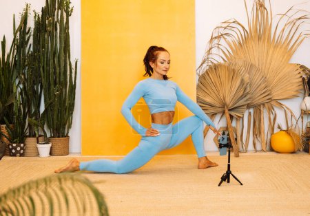 Foto de Una mujer morena muestra un entrenamiento en línea. Yoga, estiramiento, pilates. Concepto de aprendizaje a distancia y estilo de vida saludable. - Imagen libre de derechos