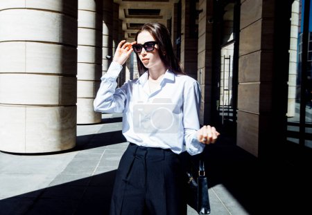 Téléchargez les photos : Portrait extérieur d'une jeune belle femme confiante aux cheveux longs et aux lunettes de soleil posant dans la rue. - en image libre de droit