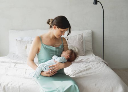 Téléchargez les photos : Maman aimante portant son nouveau-né à la maison. Portrait lumineux de maman heureuse tenant bébé endormi sur les mains. Mère étreignant son petit fils de 1 mois. - en image libre de droit