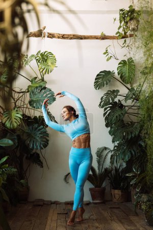 Téléchargez les photos : Brunette femme pratique le yoga à la maison parmi les fleurs. Jungle urbaine et gymnastique, yoga, pilates. Concept de style de vie. - en image libre de droit