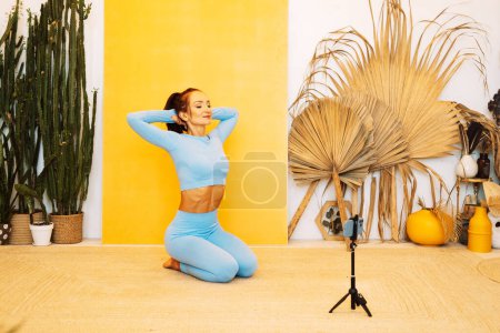 Téléchargez les photos : Une femme brune montre une séance d'entraînement en ligne. Yoga, étirement, Pilates. Concept d'enseignement à distance et mode de vie sain. - en image libre de droit