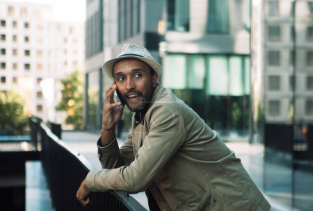 Téléchargez les photos : Un jeune homme noir en chapeau parle au téléphone, à côté d'un centre d'affaires. - en image libre de droit