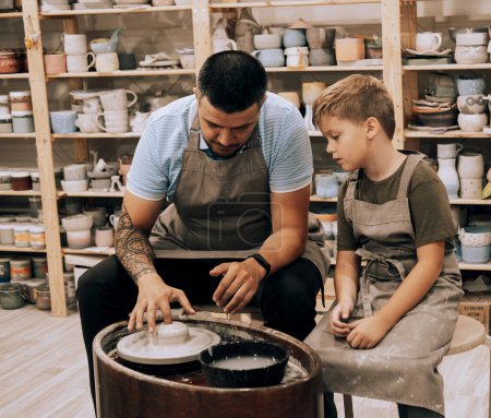 Photo for Pottering with son. Confident young man and little boy making ceramic pot on the pottery class - Royalty Free Image
