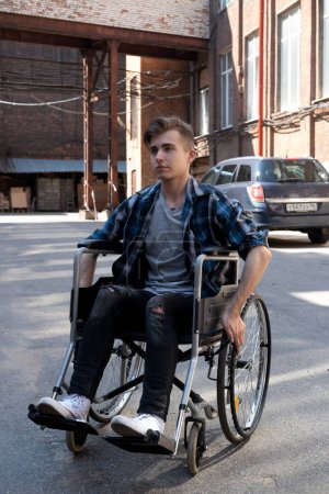 Photo for A young disabled man wearing casual sits in a wheelchair. Walk on a summer day. City background. Concept of rehabilitation, health and support for disabled people. - Royalty Free Image