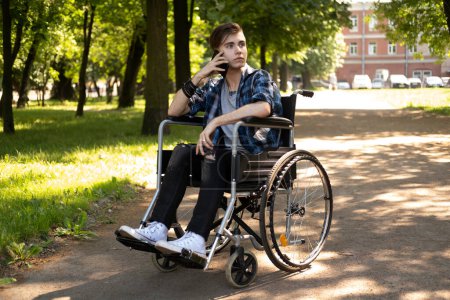 Foto de El concepto de rehabilitación, salud y apoyo a las personas con discapacidad. Un joven rubio en silla de ruedas habla por teléfono. - Imagen libre de derechos
